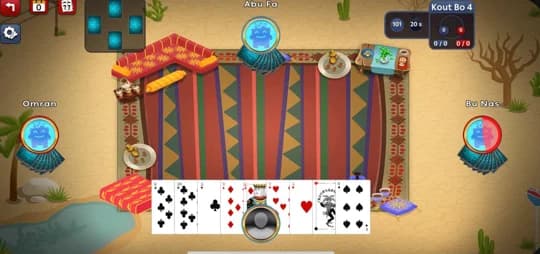 A hand of Kout in play: four players seated around a sadu rug in a desert diwaniya, cards fanned across the bottom of the screen.